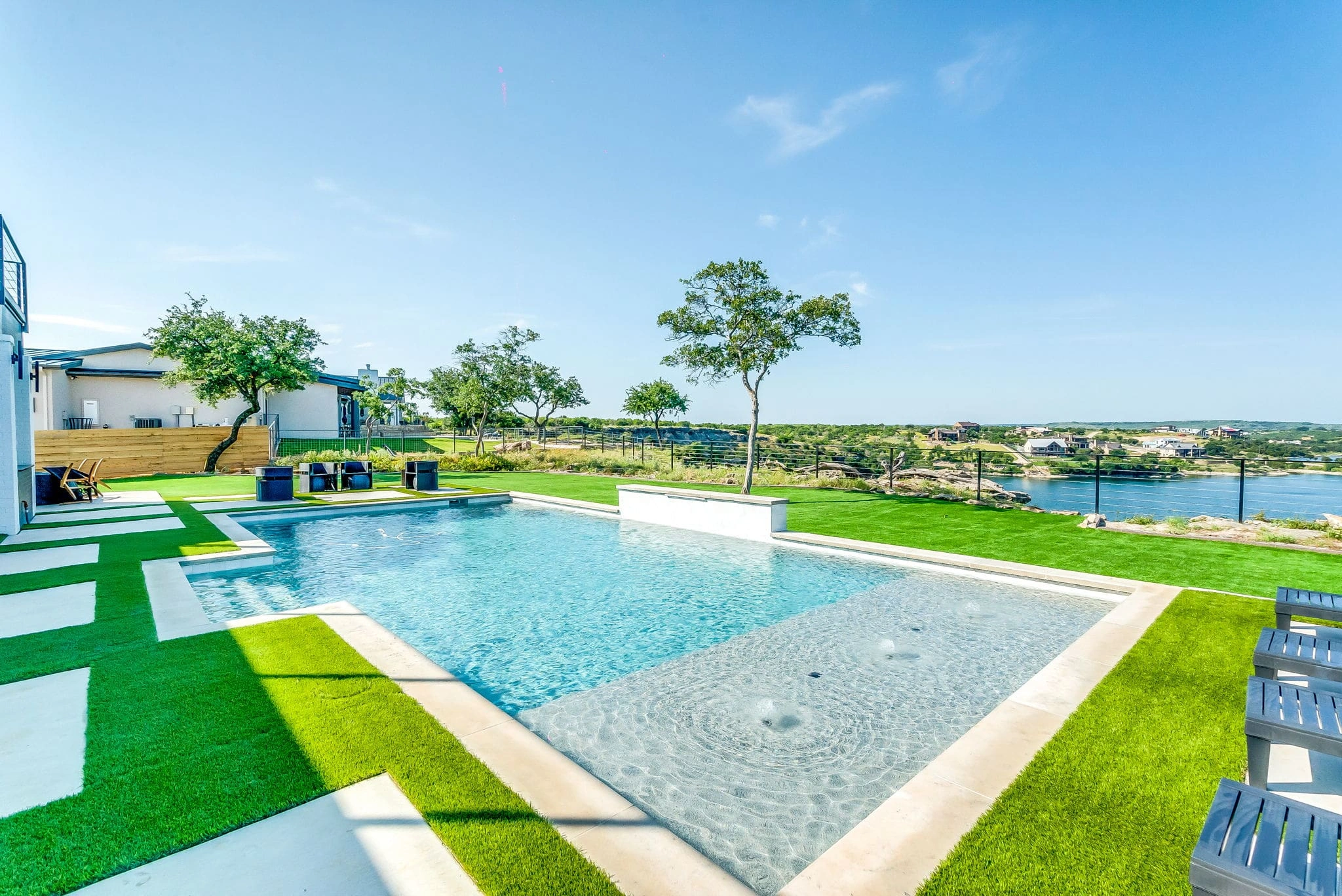 Modern pool with concrete stepping stones in turf lawn, shallow wading area with bubblers, and waterfront views