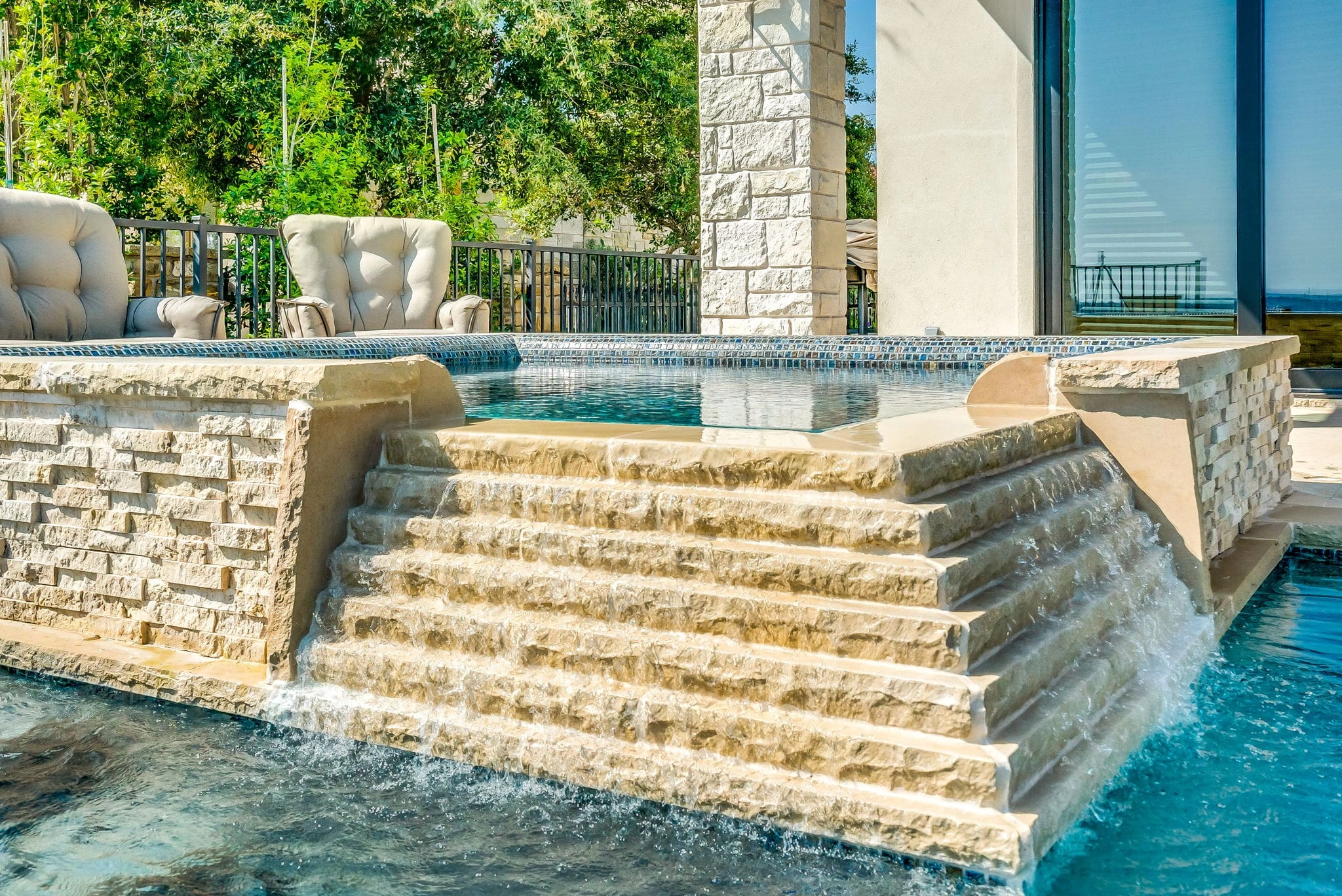 Elevated stone spa with water cascading down steps into a custom luxury pool