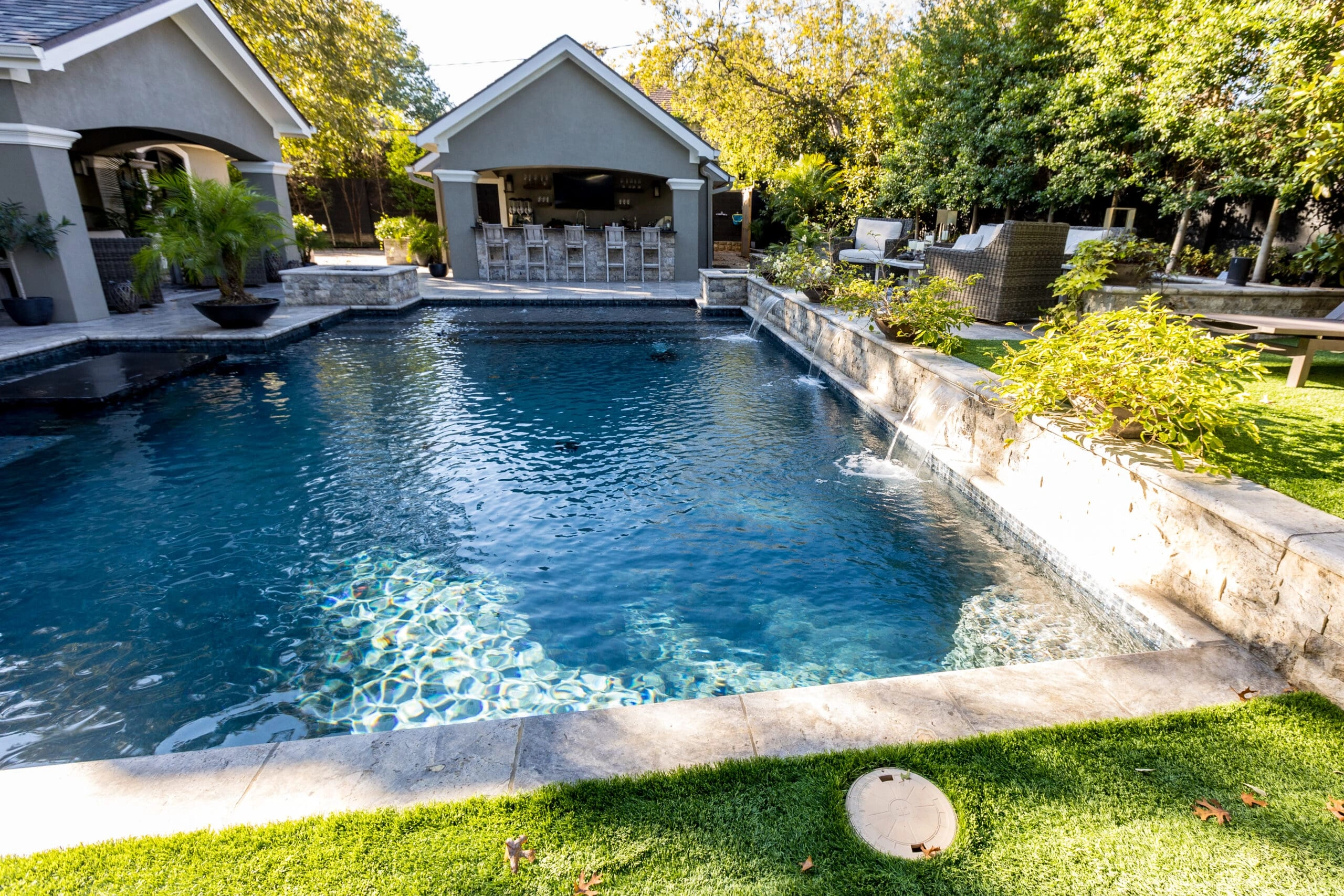 COX2-scaled Large rectangular dark-bottom pool with stone raised spa, waterfall feature, and covered outdoor bar in a landscaped backyard
