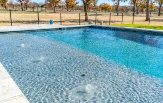 Large custom swimming pool with tanning ledge and bubbling water features under a clear blue sky