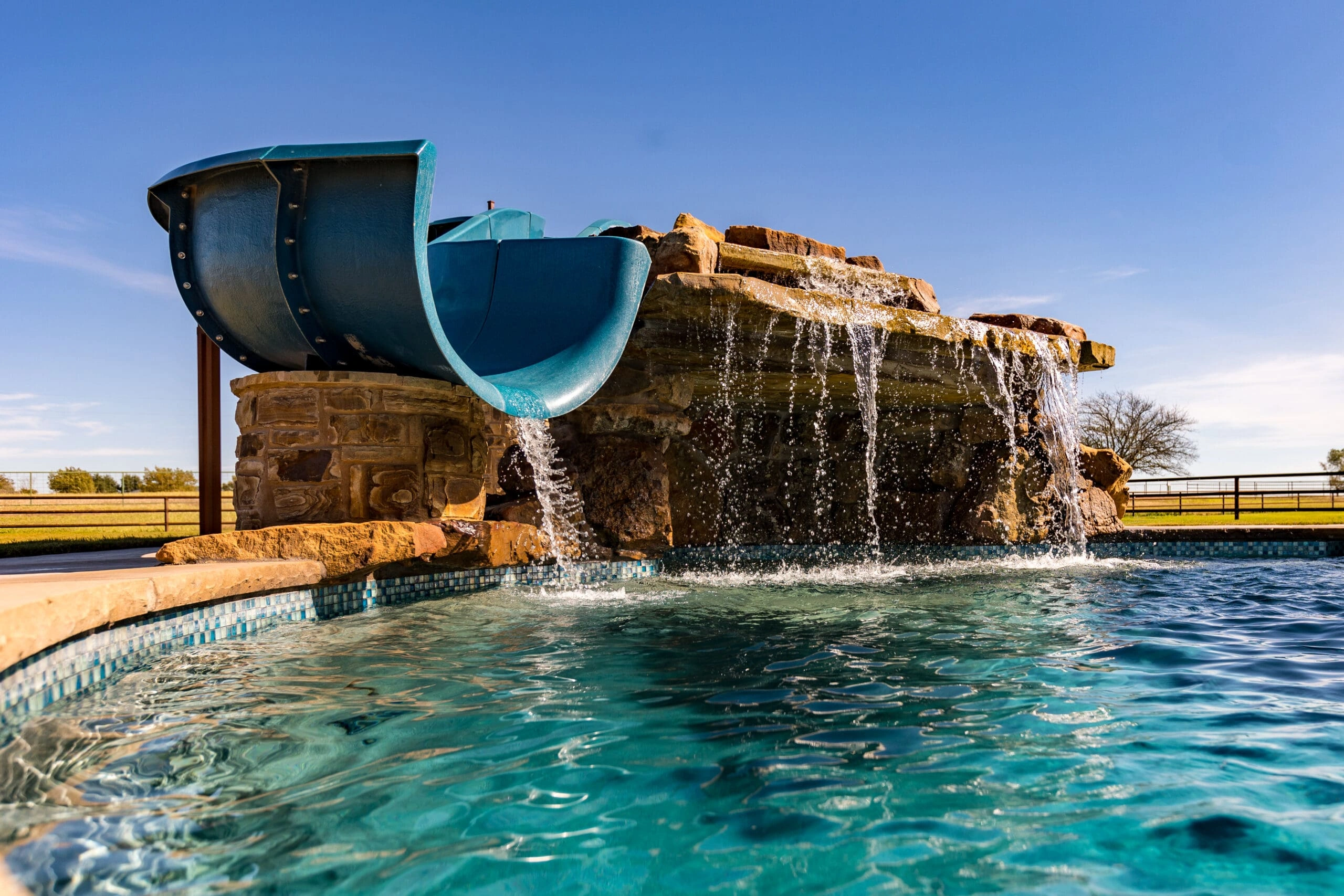 HAMPTON1-scaled Luxury pool water feature with integrated blue slide and natural stone waterfall
