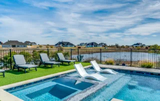 Luxury geometric pool and integrated spa with tanning ledge and lounge chairs by a lake