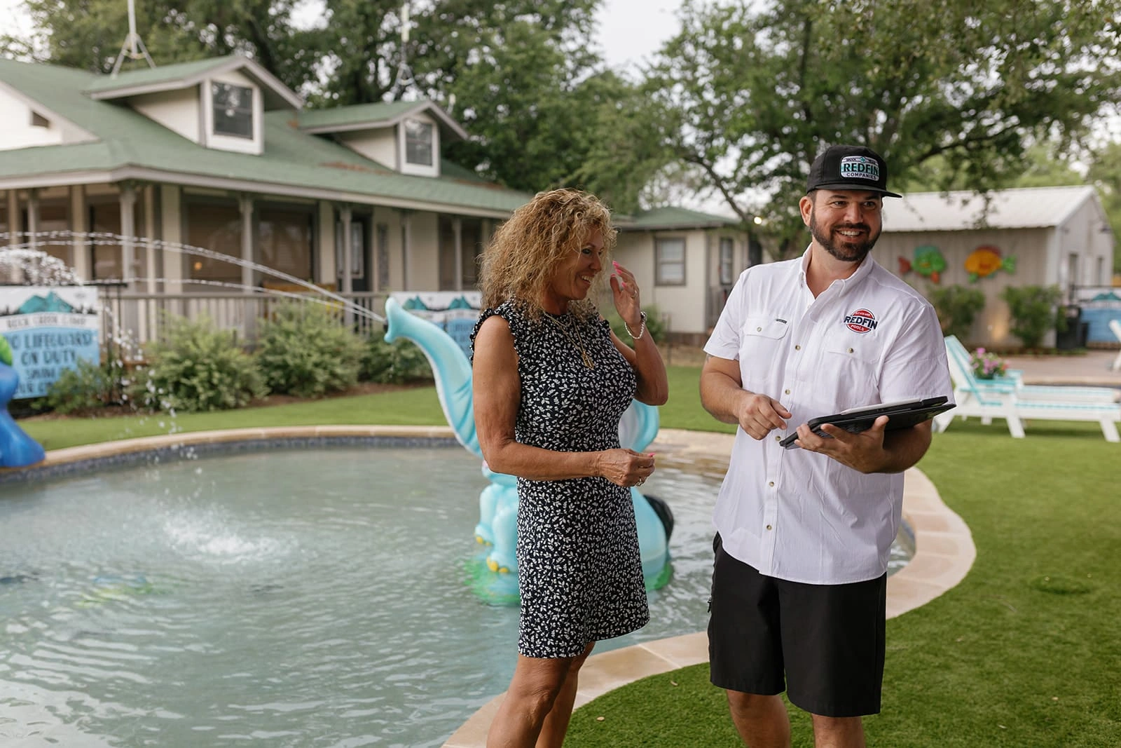 A Redfin Pools representative consulting with a homeowner beside a backyard pool with a fountain and pool floats