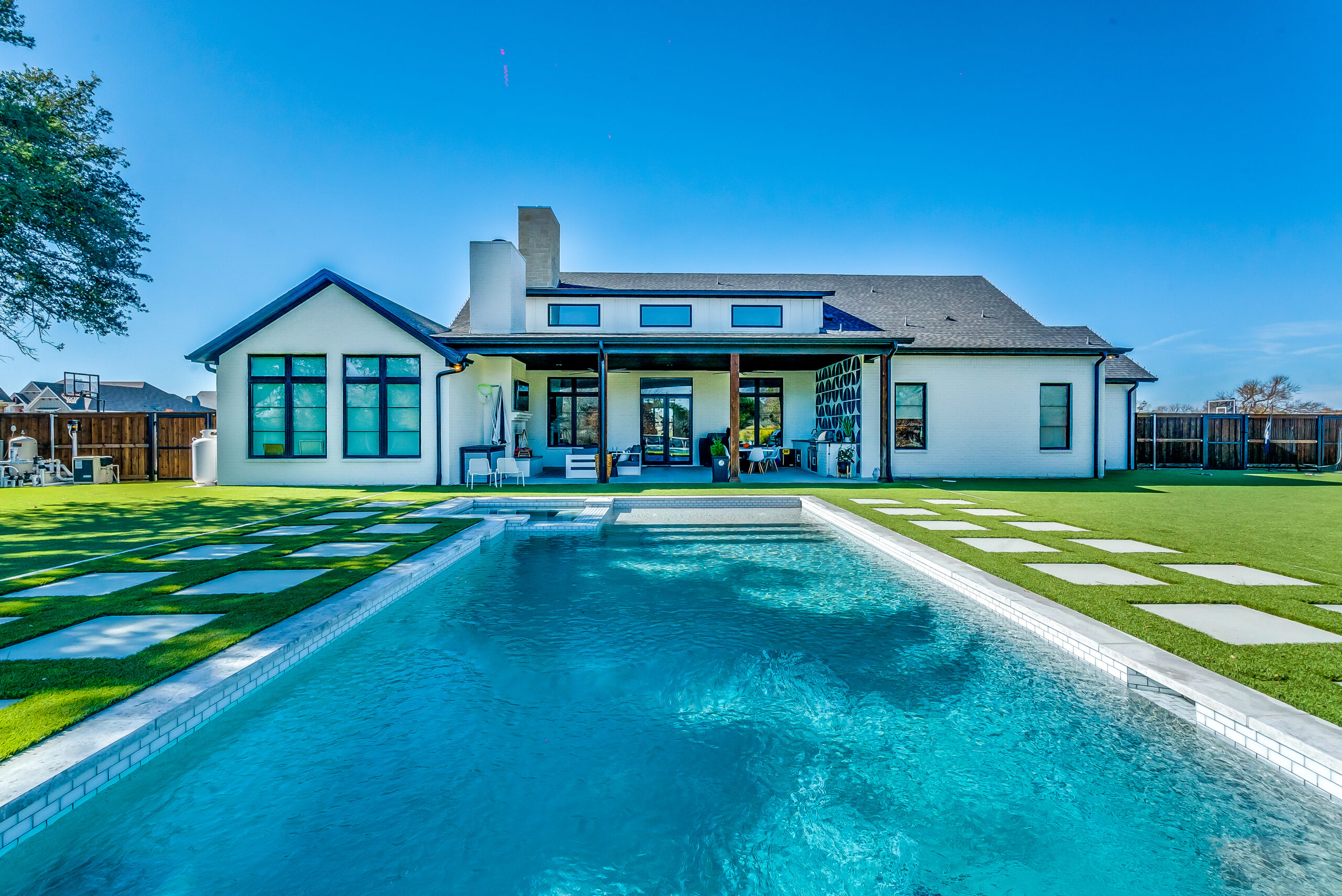 Full backyard view of a custom luxury pool with white brick house and modern landscaping