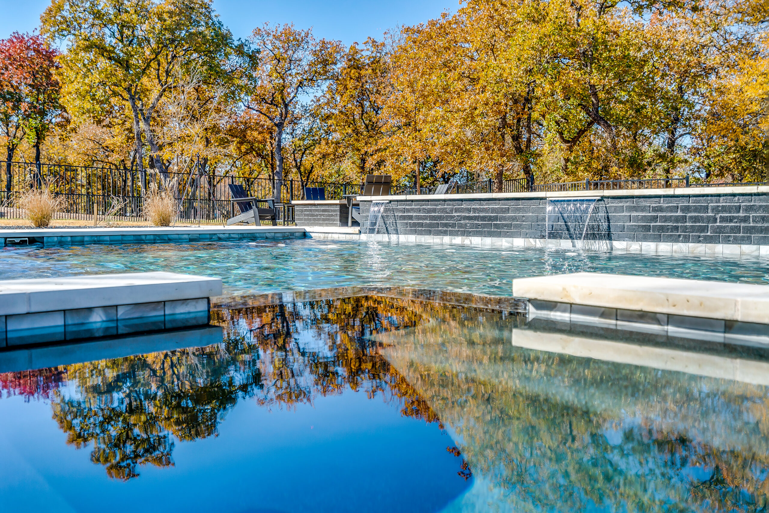 DSC03946BLENDED Modern geometric pool with dual waterfall walls and stone tanning ledges reflecting autumn trees
